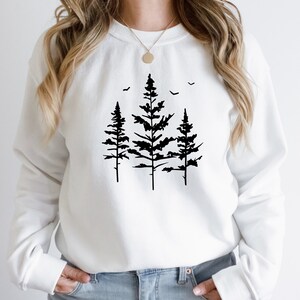 May include: White sweatshirt featuring a black silhouette of three pine trees with birds flying above them.
