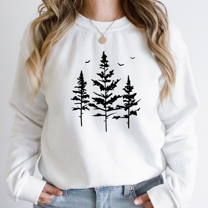 May include: White sweatshirt featuring a black silhouette of three pine trees with birds flying above them.