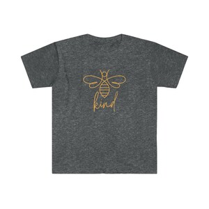 Puede incluir: Camiseta gris oscuro con un contorno dorado de abeja y la palabra "kind" en fuente cursiva. La camiseta tiene cuello redondo y mangas cortas. El dise&ntilde;o est&aacute; centrado en el pecho.