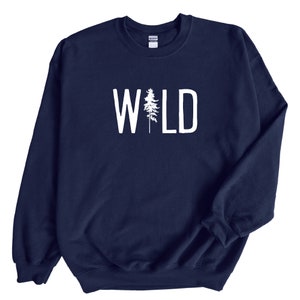 May include: A navy blue sweatshirt with the word "WILD" printed in white on the front. The word "WILD" is centered on the sweatshirt and is surrounded by a white outline. A small pine tree is incorporated into the letter "I" in the word "WILD".