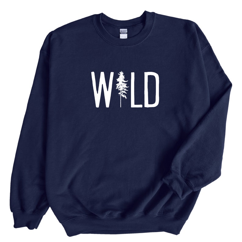 May include: A navy blue sweatshirt with the word "WILD" printed in white on the front. The word "WILD" is centered on the sweatshirt and is surrounded by a white outline. A small pine tree is incorporated into the letter "I" in the word "WILD".
