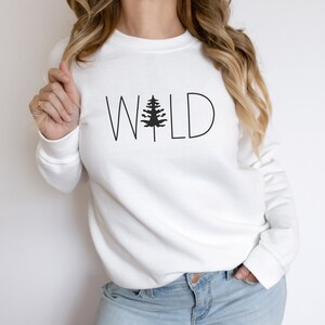 May include: White sweatshirt with a black graphic of a pine tree and the word "WILD" in black text.