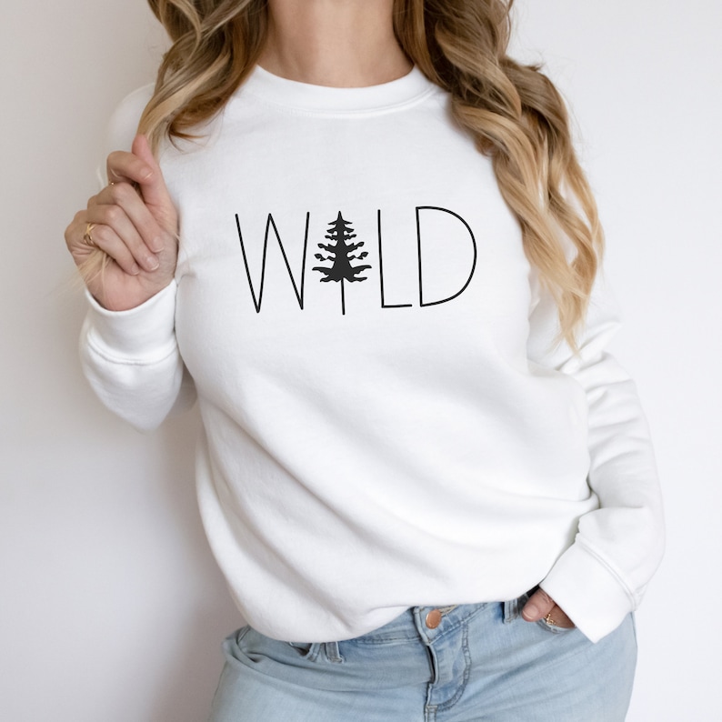 May include: White sweatshirt with a black graphic of a pine tree and the word "WILD" in black text.