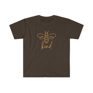 Puede incluir: Camiseta marr&oacute;n con un dise&ntilde;o minimalista de una abeja dorada y la palabra "kind" escrita a mano. El dise&ntilde;o dorado de la abeja y el texto contrastan con el fondo marr&oacute;n de la camiseta.