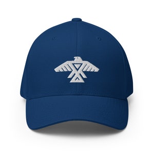 Peut inclure: Une casquette de baseball bleu marine avec un motif d'aigle brodé en blanc. L'aigle est stylisé avec un motif géométrique et une forme triangulaire au centre.