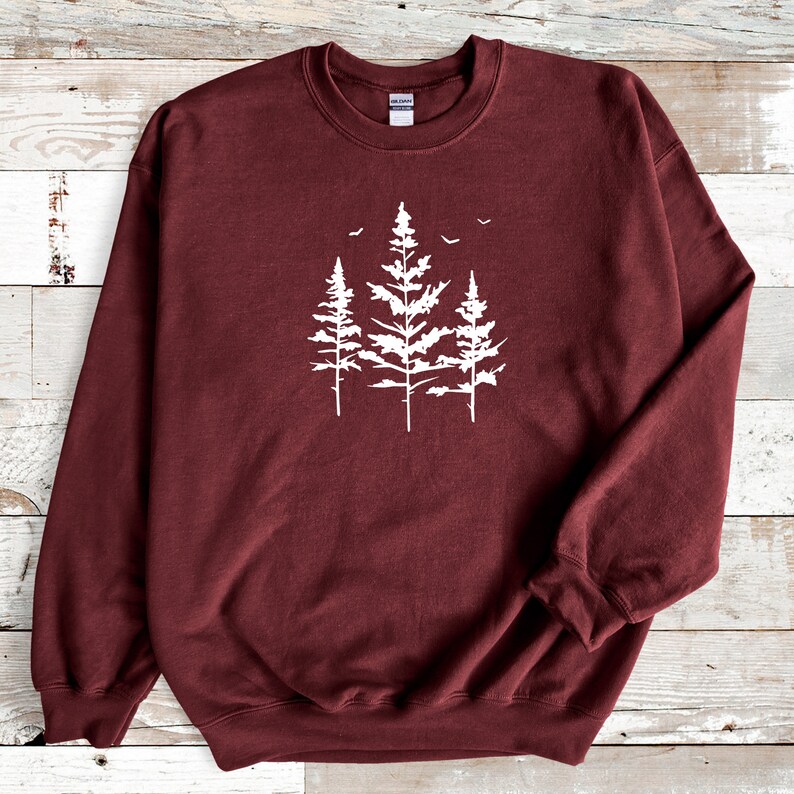 May include: A maroon sweatshirt featuring a white silhouette of three pine trees with birds flying above them.