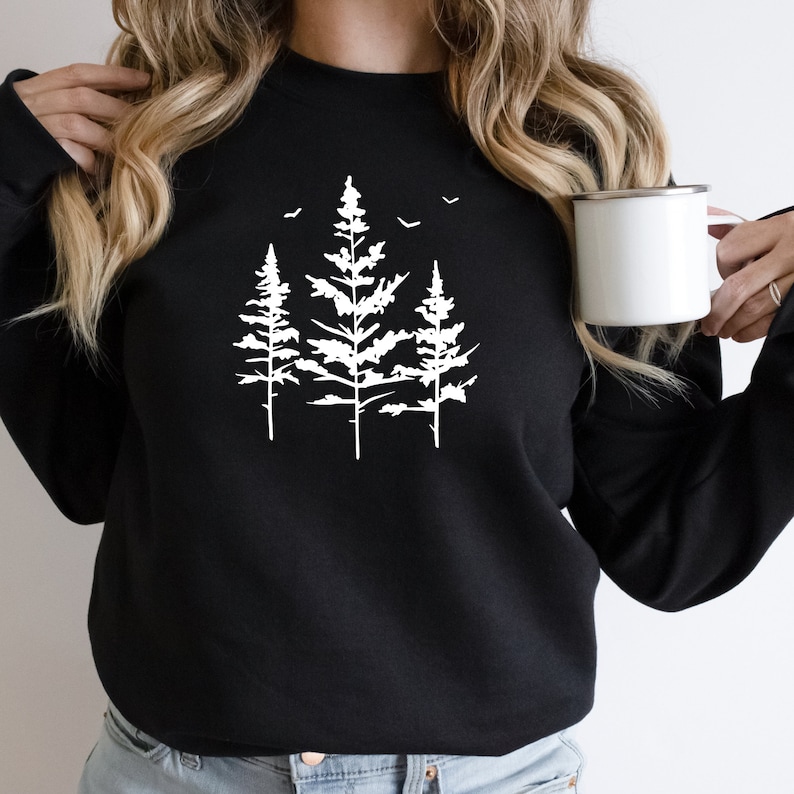 May include: Black sweatshirt featuring a white graphic of three pine trees with birds flying above them.