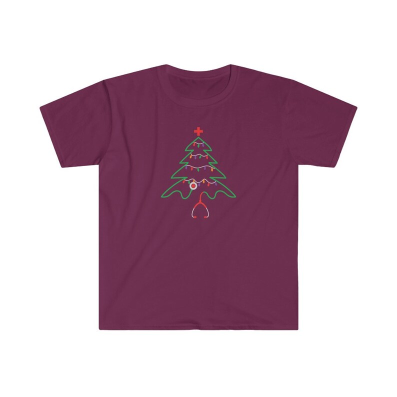 以下が含まれることがあります： マロン色のTシャツに、緑色のクリスマスツリーのデザインが施されています。ツリーは、赤と白のオーナメント、赤い十字架、聴診器で飾られています。