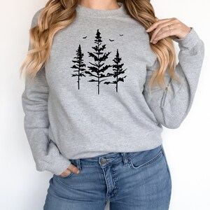 May include: A grey sweatshirt with a black silhouette of three pine trees and flying birds on the front.