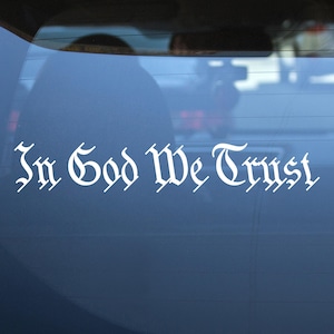 May include: A white vinyl sticker with the words "In God We Trust" in a stylized font, applied to the back window of a blue car.