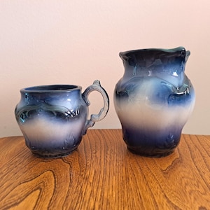 May include: A blue and white ceramic creamer and sugar set with a floral design. The creamer has a handle and the sugar bowl has a lid.