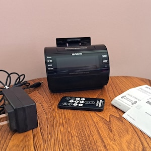 May include: A black Sony clock radio with a digital display, a remote control, and a power adapter. The clock radio has a CD player, an AM/FM radio, and an alarm clock. The remote control has buttons for volume, play/pause, and other functions. The power adapter has a black cord and a plug.