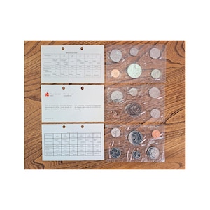 May include: A collection of Canadian coins in clear plastic packaging, displayed on a wooden surface. The set includes various denominations, with accompanying informational cards. The coins are in various sizes and colours, including silver and copper.