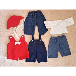 May include: A set of five clothing items for a doll, including a red hat, a red overall with a white bow, a blue overall, a pair of blue denim shorts, and a white button-up shirt.