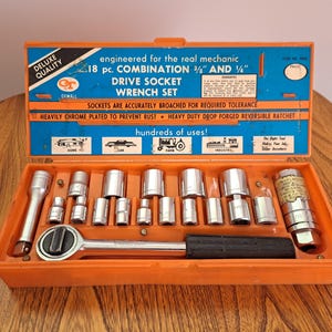 May include: An orange toolbox with a blue top contains a 18-piece drive socket wrench set. The box has text that reads "Deluxe Quality" and "Engineered for the real mechanic." The set includes various sockets and a reversible ratchet.
