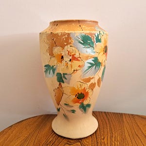 May include: A vintage ceramic vase with a floral design. The vase is painted with yellow, orange, and green flowers on a cream background.
