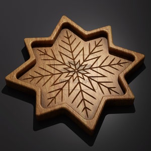 Può includere: Un vassoio di legno a forma di stella con un motivo a fiocco di neve intagliato. Il vassoio è marrone e ha una finitura in legno naturale.