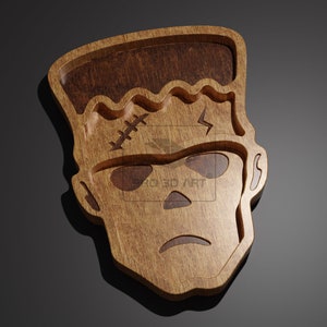May include: A wooden tray shaped like Frankenstein's face. The tray has a stitched scar, a bolt, and a furrowed brow.