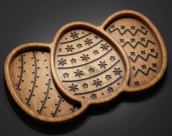 Könnte beinhalten: Ein Tablett aus Holz in Form von drei Ostereiern, jedes mit einem anderen geschnitzten Design. Das Tablett ist aus hellbraunem Holz gefertigt und hat eine natürliche Oberfläche.