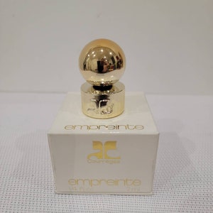 May include: A small bottle of Courr&egrave;ges Empreinte perfume. The bottle is clear glass with a gold cap and a gold ball on top. The bottle is sitting on a white box with the words "Courr&egrave;ges Empreinte" printed on it. The box is 1/4 fl oz or 7 ml.