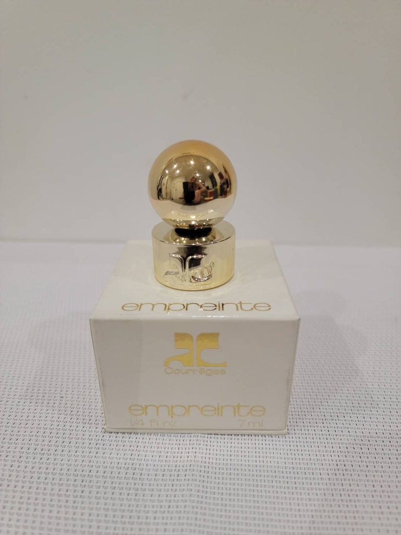 May include: A small bottle of Courr&egrave;ges Empreinte perfume. The bottle is clear glass with a gold cap and a gold ball on top. The bottle is sitting on a white box with the words "Courr&egrave;ges Empreinte" printed on it. The box is 1/4 fl oz or 7 ml.