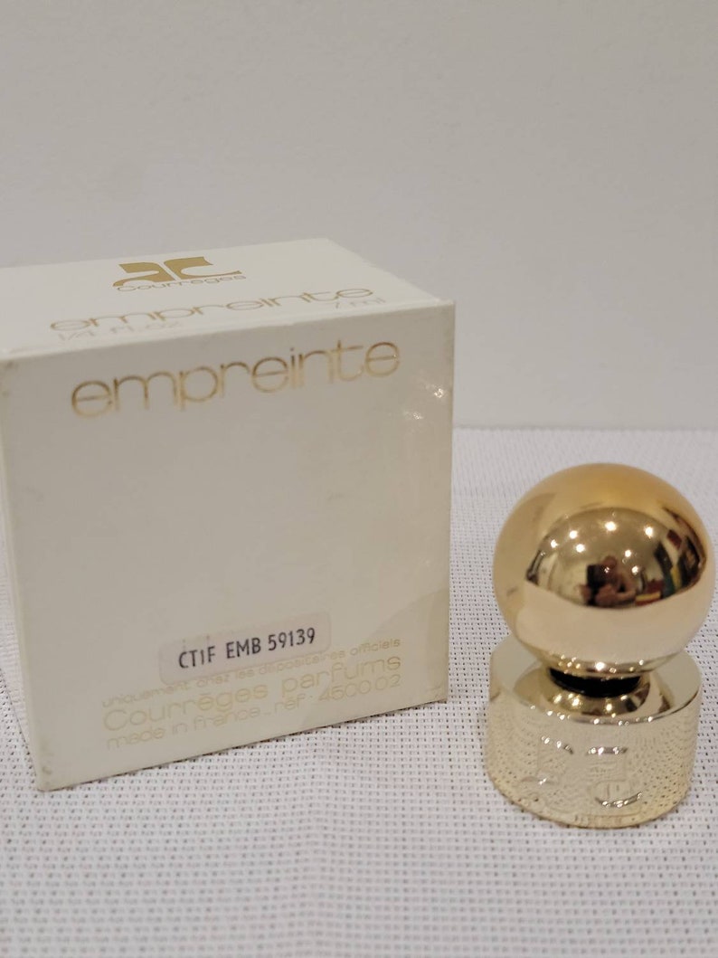 May include: A white box with gold lettering that reads "Courr&egrave;ges Empreinte" and "CTIF EMB 59139". The box is for a perfume bottle with a gold ball stopper.