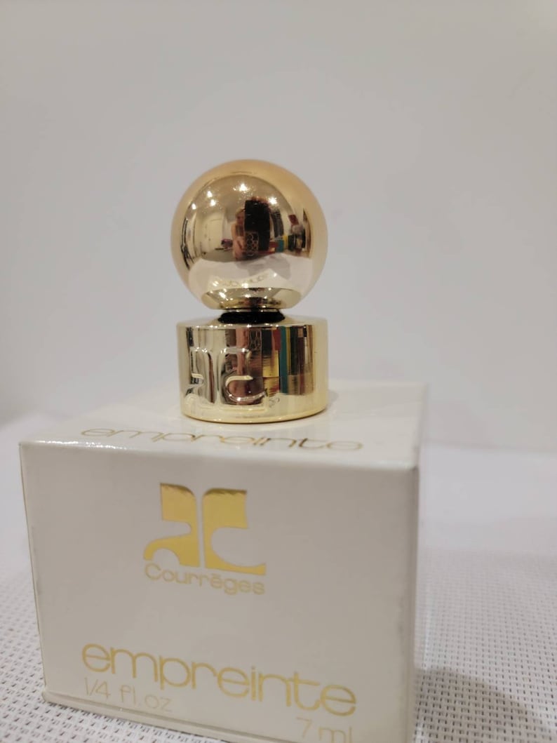 May include: A small bottle of Courr&egrave;ges Empreinte perfume. The bottle is clear glass with a gold cap and a gold ball on top. The box is white with gold lettering. The bottle contains 1/4 fl oz (7 ml) of perfume.