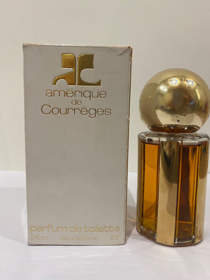 May include: A white box with gold lettering that reads "amerique de Courr&egrave;ges" and "parfum de toilette 2 fl. oz. natural spray 83&deg;". The box is next to a clear glass bottle of perfume with a gold cap and a gold band around the bottle.