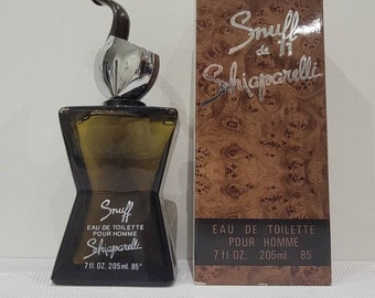 May include: A brown glass bottle of Snuff de Schiaparelli Eau de Toilette for men. The bottle has a unique design with a curved spout and a silver cap. The bottle is labeled with the name of the fragrance and the size, 7 fl. oz. 205 ml. 85°.