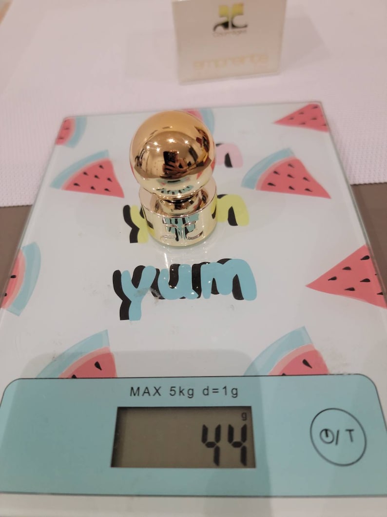 May include: A gold-colored bottle stopper on a digital scale with a watermelon print. The scale reads 44 grams.