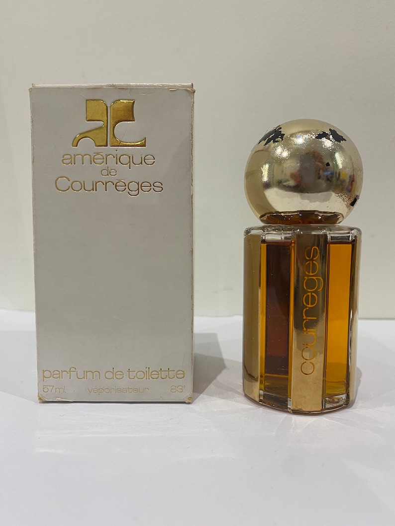 May include: A white box with gold lettering that reads "amerique de Courreges" and "parfum de toilette 57ml vaporisateur 83'" with a clear glass bottle of perfume with a gold cap and a gold label that reads "Courreges".