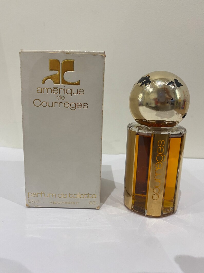 May include: A white box with gold lettering that reads "amerique de Courreges" and "parfum de toilette 57ml vaporisateur 83". A clear glass bottle with a gold cap and gold lettering that reads "Courreges" is in front of the box.