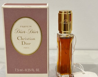 Könnte beinhalten: Ein kleines Fläschchen Dior-Dior Parfum von Christian Dior in einer durchsichtigen Glasflasche mit goldenem Verschluss. Die Flasche steht auf einer weißen Oberfläche mit einer weißen Schachtel und einem weißen Etikett. Die Schachtel ist rosa und weiß und trägt den Aufdruck "Parfum Dior-Dior Christian Dior Paris". Das Etikett trägt den Aufdruck "Parfums Christian Dior Paris". Die Flasche enthält 7,5 ml oder 0,25 fl oz Parfum.