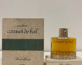 May include: A small bottle of perfume called "Carnet de Bal" by Revillon Paris. The bottle is clear glass with a gold cap and a gold label. The box is white with a green stripe and a gold pattern.