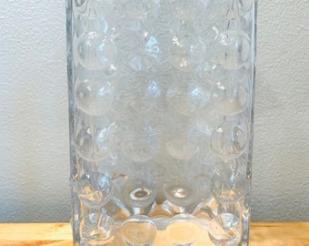 May include: A clear glass vase with a textured, bubble-like design. The vase is rectangular in shape and has a wide opening.