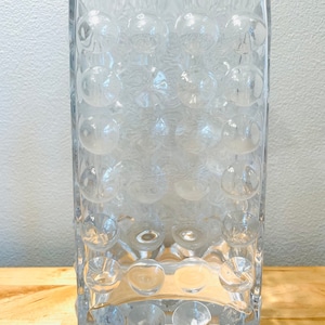 May include: A clear glass vase with a textured, bubble-like design. The vase is rectangular in shape and has a wide opening.