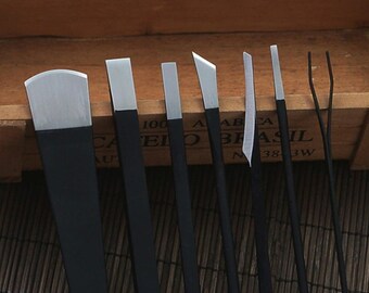 May include: Set of eight black handled nail tools with silver metal tips. The tools include a cuticle pusher, a nail file, a nail clipper, and other tools for nail care.