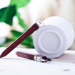 May include: Two wooden tools with metal clips for grafting plants. The tools are on a white surface.