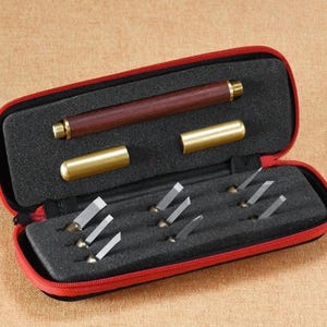 May include: A red carrying case with a zipper closure holds a set of 8 small carving tools with wooden handles and a larger carving tool with a wooden handle and a brass cap. The tools are arranged in a foam-lined case.