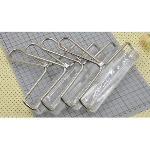 May include: Four silver rolling pins with clear plastic rollers. The rolling pins are stacked on top of each other and are on a gray and white grid.