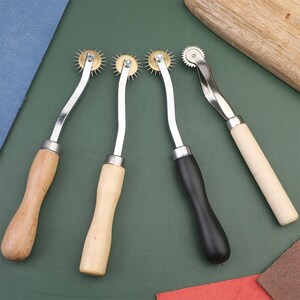 May include: Three leather sewing tools with wooden handles and metal wheels. The wheels have small, sharp points.