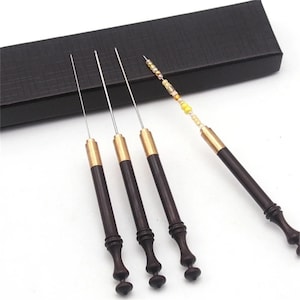 May include: Set of four wooden beading tools with gold accents and thin metal needles. The tools are arranged in a row on a black surface.