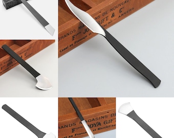 May include: Four black handled tools with silver blades. The tools have a rounded tip and a sharp edge. The tools are on a wooden surface with text in French.