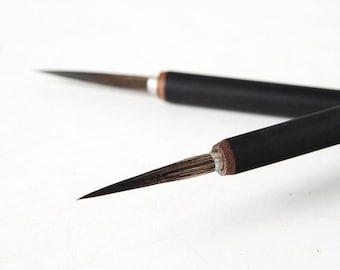 以下が含まれることがあります： 黒色の柄と茶色の毛を持つ、2本の筆のクローズアップ。筆は非常に細く、先が尖っています。