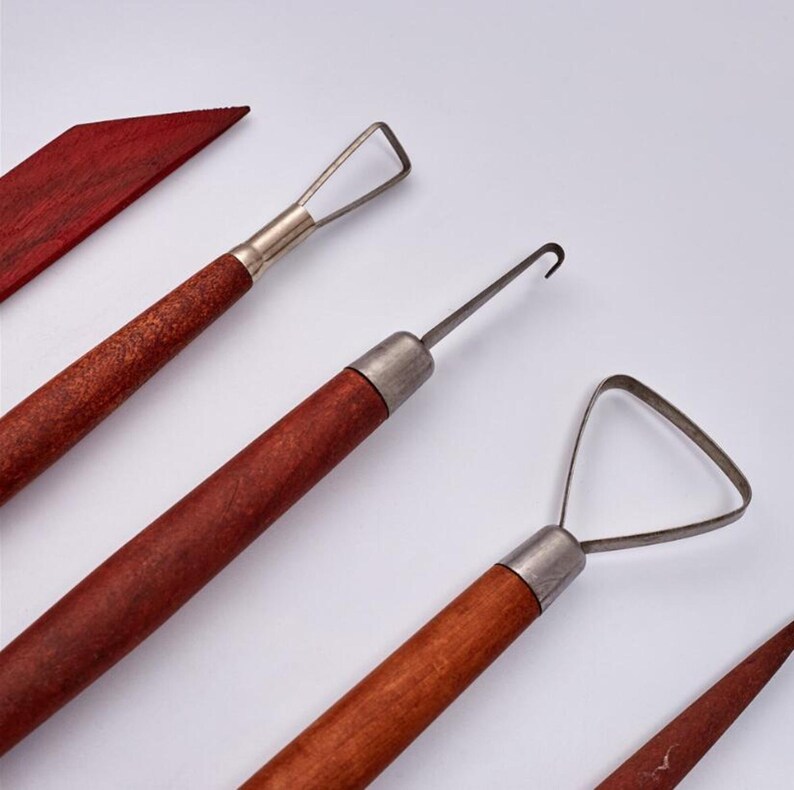 Peut inclure: Quatre outils de sculpture avec des manches en bois. Les outils ont des embouts m&eacute;talliques diff&eacute;rents pour fa&ccedil;onner l'argile. Les outils sont sur un fond blanc.