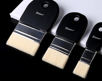 Puede incluir: Tres pinceles con mango negro y cerdas de color natural. Los pinceles están dispuestos en fila, disminuyendo de tamaño. Cada pincel tiene una virola de metal plateado y la palabra "Giorgione" impresa en el mango.