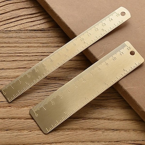 May include: Two gold-colored metal rulers with markings in inches. The rulers are 12 inches long and have a hole at the top.