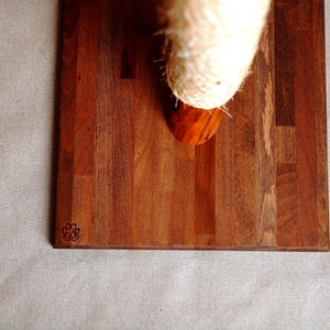 May include: A wooden cat scratching post with a natural sisal rope covered post. The base is made of dark wood with a paw print logo.