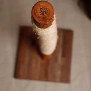 May include: A wooden cat scratching post with a natural rope covering and a paw print design on the top. The post is mounted on a wooden base.