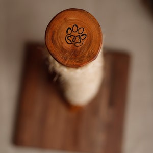 May include: A wooden cat scratching post with a paw print design on the top. The post is wrapped in sisal rope and is mounted on a wooden base.